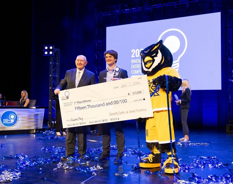 Ákos Vida holding the ,000 first-place check made out to AdaptaPlay, next to a Kennesaw State mascot.