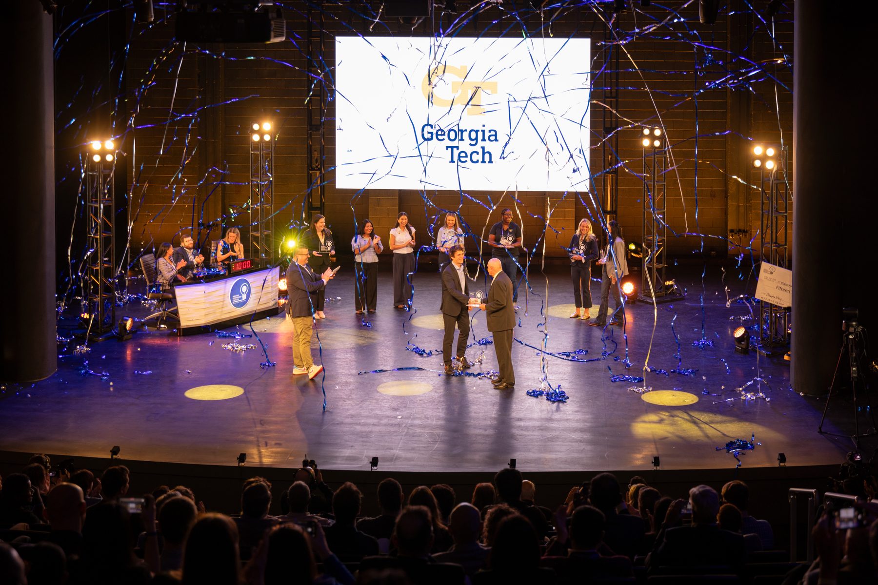 Ákos Vida receiving the first-place award on stage under falling streamers, with the Georgia Tech logo on the screen behind.